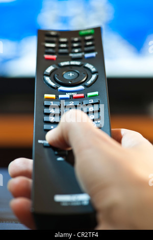 Mano che tiene la televisione telecomando premendo i pulsanti Foto Stock