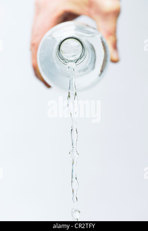 Mano versando acqua minerale da una bottiglia di vetro contro uno sfondo bianco Foto Stock