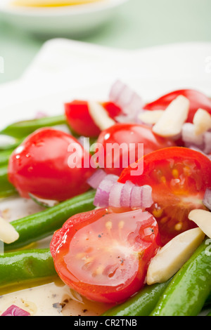 Insalata di fagioli verdi, pomodori e cipolla rossa, mandorle e limone Insalata, disposti su una piastra bianca. Foto Stock