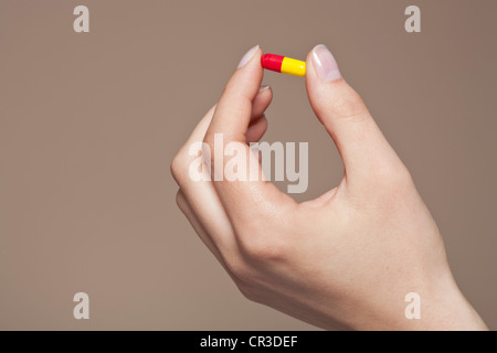 La mano di una giovane donna che mantiene una pillola, capsula tra le dita Foto Stock