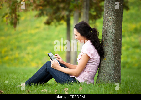 Giovane donna appoggiata contro un albero, utilizzando un tablet PC Foto Stock