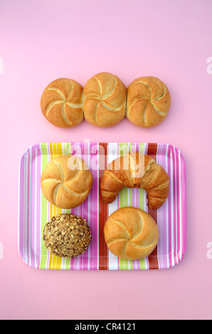 Panini accanto a un croissant e un panino, un rotolo di integrale e un rotolo di multigrain su un tessuto a righe, vassoio rosa Foto Stock