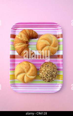 Un croissant e un panino, un rotolo di integrale e un rotolo di multigrain su un tessuto a righe, vassoio rosa Foto Stock