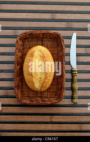 Un unico rotolo di pane in un cestino, coltello colazione Foto Stock