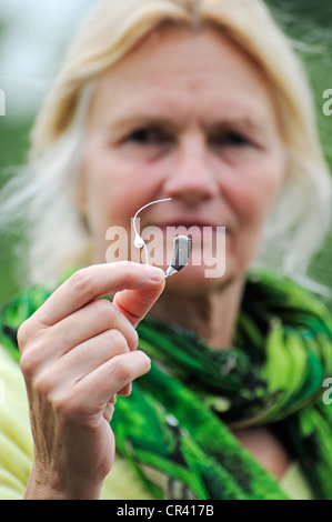 Moderno piccolo hearing aid nelle mani di una donna, la durezza dell'udito Foto Stock