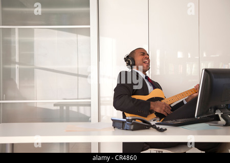 Imprenditore nero a suonare la chitarra alla scrivania Foto Stock