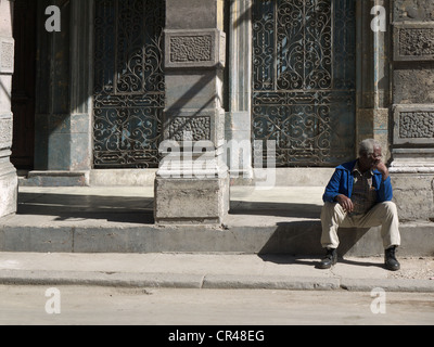 Di carnagione scura anziani uomo cubano annoiato seduto sulle scale di fronte a un vecchio edificio facciata, l'Avana, Cuba, America Latina Foto Stock