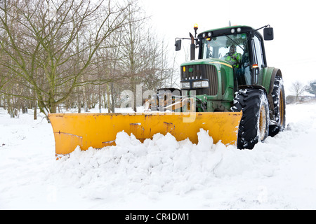 Un trattore equipaggiato con un frontale montato Snow Plough cancellazione di una strada di neve nel Regno Unito Foto Stock