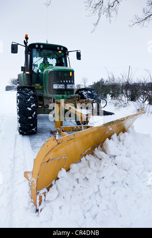 Un trattore equipaggiato con un frontale montato Snow Plough cancellazione di una strada di neve nel Regno Unito Foto Stock