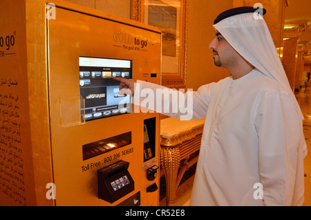 Uomo locale che indossa una dishdasha, tradizionale tunica bianca, nella parte anteriore della macchina in oro "Gold per andare' nell'Emirates Palace Hotel Foto Stock