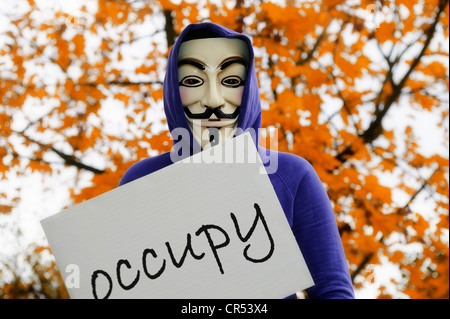 Uomo che indossa la maschera di Guy Fawkes utilizzato da occupare il movimento tenendo un segno di protesta, protestando contro il potere delle banche Foto Stock