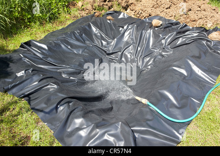Utilizzando un tubo flessibile per riempire un foro rivestito con un rivestimento di stagno di creare uno stagno in un giardino nel Regno Unito Foto Stock