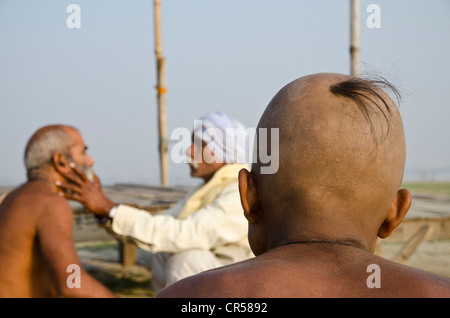 La rasatura della testa come parte di un rituale religioso, eseguita a Sangam, alla confluenza dei fiumi Santo Gange Foto Stock