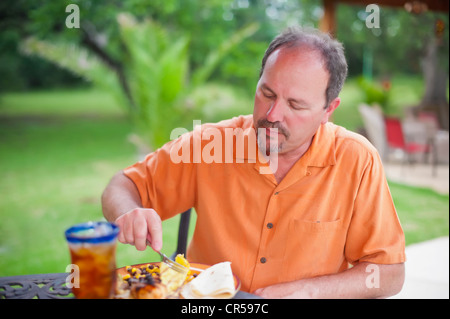 Uomo di mangiare al barbecue nel cortile Foto Stock