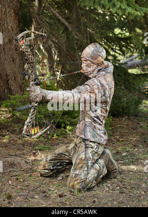 Close-up bow hunter vestito in camuffamento tirando arco tornare nel bosco Foto Stock