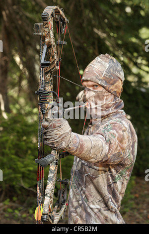 Close-up bow hunter vestito in camuffamento tirando arco tornare nel bosco Foto Stock