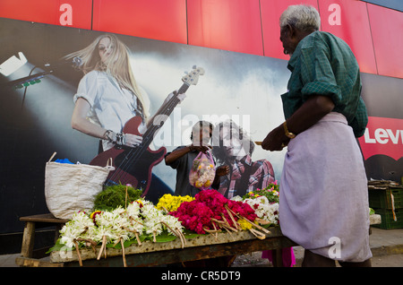 Flowerseller con il suo negozio di impostare nella parte anteriore di un concerto di poster, Madurai, Tamil Nadu, India, Asia Foto Stock