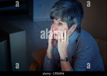 Donna seduta davanti al suo televisore guardando le notizie, scioccato Foto Stock