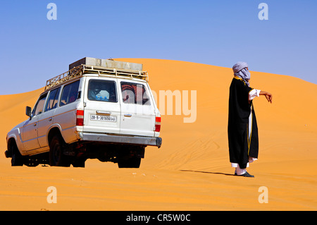 Uomo arabo in abito tradizionale in piedi accanto al suo veicolo fuoristrada nel deserto, Ubari Mare di Sabbia, Sahara, Libia, Africa Foto Stock