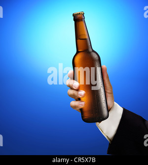 Bottiglia di birra in una mano d'uomo su uno sfondo blu. Foto Stock