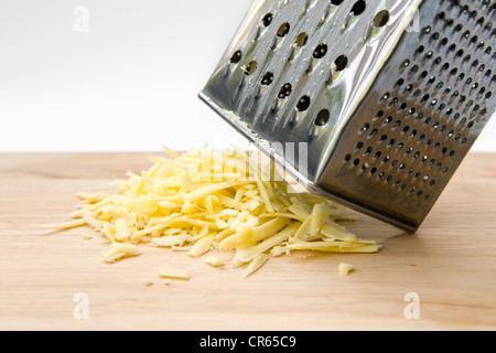 Formaggio grattugiato con la grattugia sul tagliere di legno contro uno sfondo bianco Foto Stock