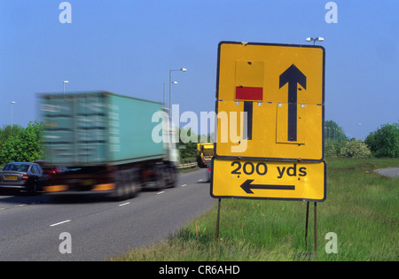 Autocarro passando un cartello di segnalazione di chiusa corsia a sinistra proseguendo sulla strada a doppia carreggiata uk Foto Stock