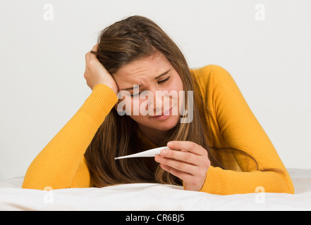 Ragazza adolescente guardando il termometro contro uno sfondo bianco Foto Stock