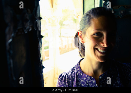 India Rajasthan, Jodhpur, giovane donna in piedi dalla vecchia finestra in Jodhpur Fort, sorridente Foto Stock