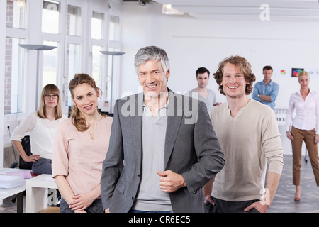 In Germania, in Baviera, Monaco di Baviera, uomo maturo con i colleghi in piedi in ufficio, sorridente Foto Stock