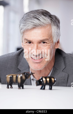 In Germania, in Baviera, Monaco di Baviera, uomo maturo con bull e bear figurine, sorridente, ritratto Foto Stock