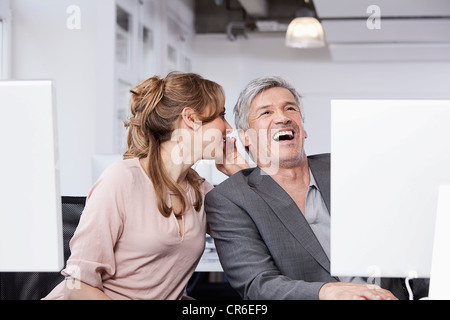 In Germania, in Baviera, Monaco di Baviera, Donna whispering nell uomo l orecchio in office Foto Stock