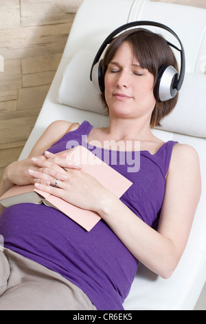 In Germania, in Renania settentrionale-Vestfalia, donna incinta con libro e ascolto di musica Foto Stock