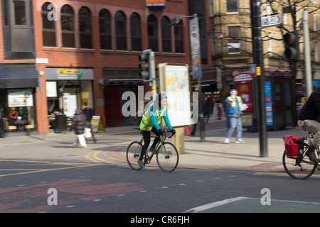 Giovani femmine ciclista di Deansgate, Manchester. Indossa un hi-vis giubbotti di sicurezza, guanti e casco del ciclo. Foto Stock