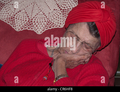 Senior donna prendendo un pisolino in una sedia rossa Foto Stock