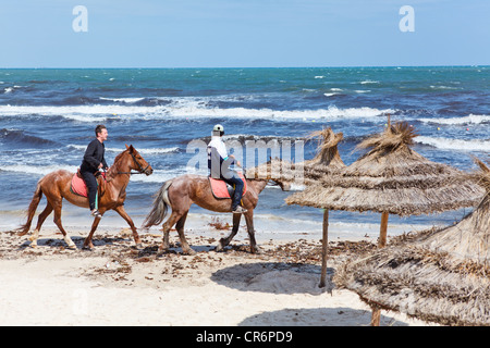 Persone su cavalli passeggiate sul lungomare di mare. Spiaggia di sabbia in Tunisia. I turisti di equitazione per denaro. Foto Stock