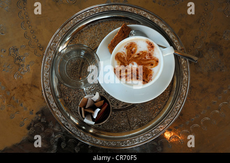 Tazza di cappuccino, vetro di acqua e di bustine di zucchero servita su un round tablet in argento con incisioni, Vienna, Austria, Europa Foto Stock