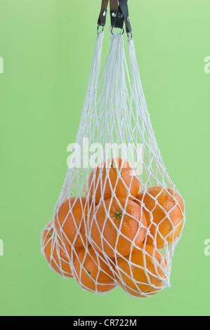 Arance in borsa a rete contro lo sfondo di colore verde, vicino fino Foto Stock