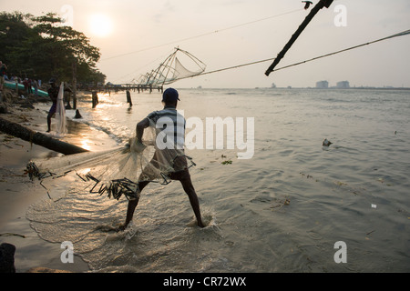 L'uomo la colata di una rete da pesca accanto alla Cinese reti da pesca al tramonto, Fort Cochin, Kochi (Cochin), Kerala, India Foto Stock