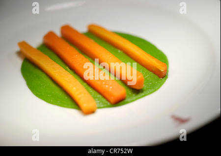 Un trito di bastoncini di carote in linee su un letto di piselli cedevole su una piastra bianca in un ristorante Foto Stock