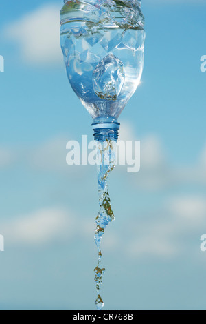 Versando acqua potabile da una bottiglia di plastica contro un cielo blu Foto Stock