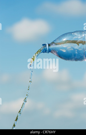 Versando acqua potabile da una bottiglia di plastica contro un cielo blu Foto Stock