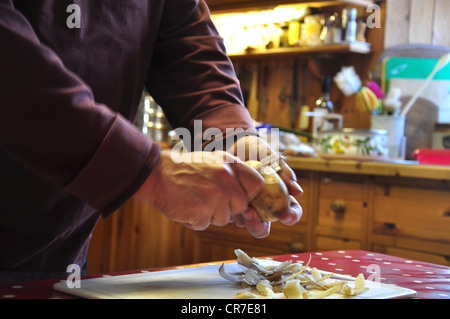 Un uomo pelare una patata in una cucina REGNO UNITO Foto Stock