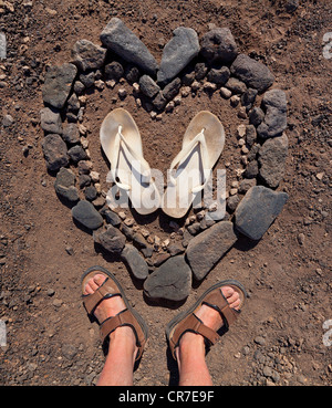 Cuore fatte di gusci e flip-flop, sandali, piedi, spiaggia rocciosa di El Puertito de la Cruz, punta meridionale dell'isola di Foto Stock