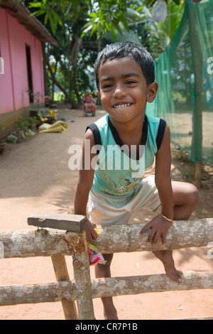 Ragazzo sorridente arrampicata su un recinto con la loro madre seduti dietro, Kanjippadom, vicino a Alappuzha (Alleppey), Kerala, India Foto Stock