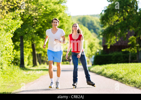 Coppia giovane - uomo e donna - facendo sport all'aperto, egli è il jogging mentre ella è palettatura a rullo Foto Stock