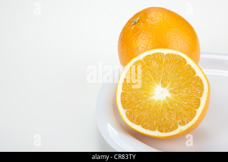 Due le arance (Citrus sinensis), un frutto intero e una metà del frutto, su una piastra bianca Foto Stock