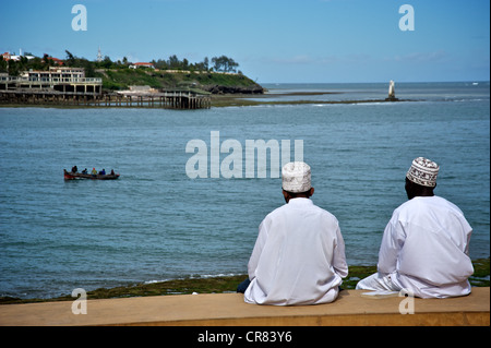 Due uomini del Kenya da dietro, seduti su una parete esterna di Fort Jesus con oceano di fronte, Mombasa, in Kenya, Africa orientale Foto Stock