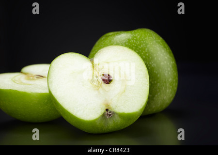 Due verdi le mele Granny Smith, 1 mela intera e una mela tagliata a metà, nero su lastra di vetro Foto Stock