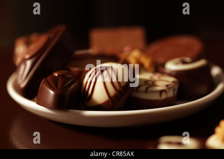 Cioccolatini su un piatto bianco al buio su un sfondo marrone Foto Stock