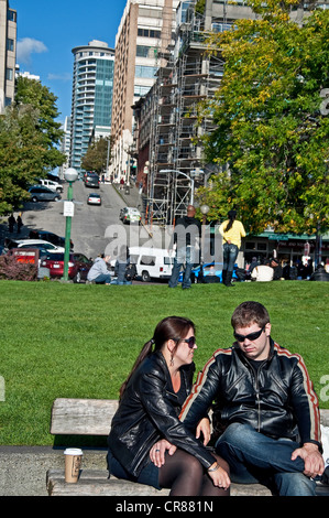 Giovane coppia caucasica, entrambi indossano giacche di pelle nera sono seduta su una panchina e parlando con il paesaggio dietro di loro. Foto Stock